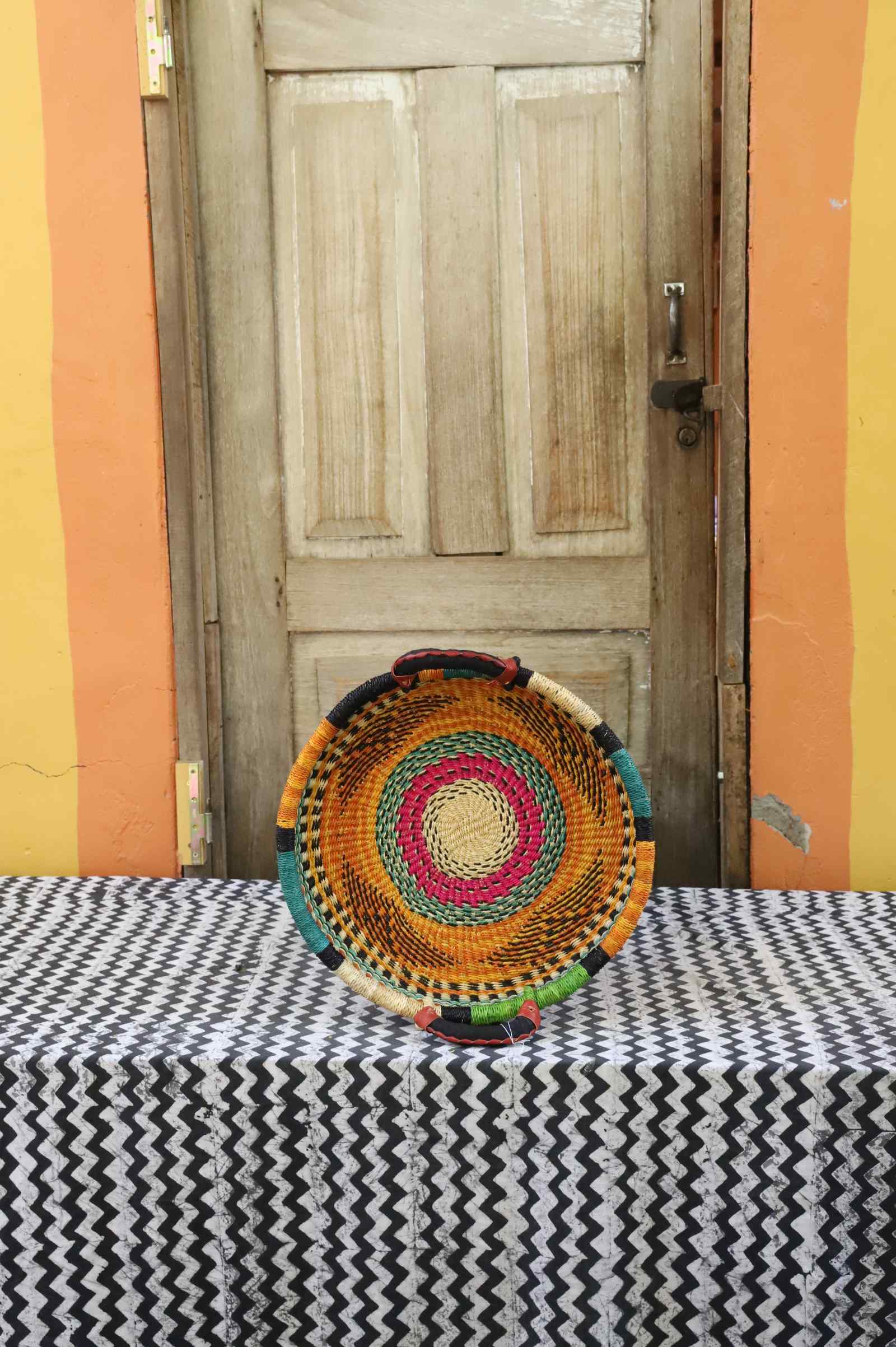 Handwoven Bolga wall tray disc with fine yellow, pink and black concentric bands.