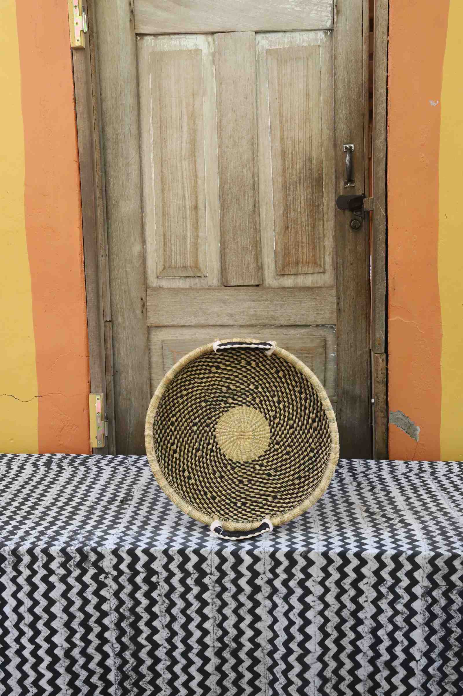 Handwoven Bolga wall tray disc in dark straw with a yellow centre dot.
