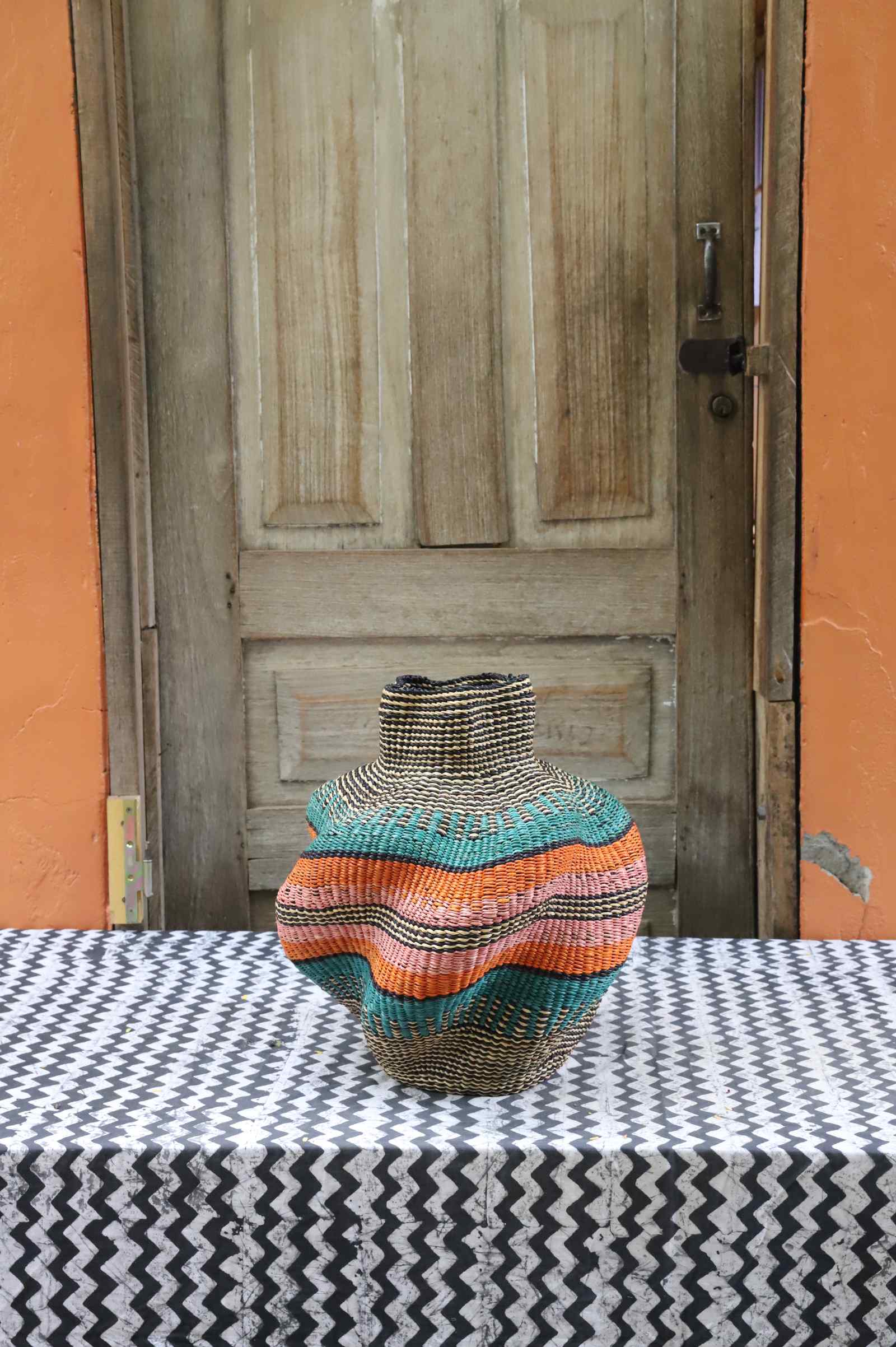 Handwoven Bolga art basket in a rounded pot shape with dark natural body and orange and teal central bands.