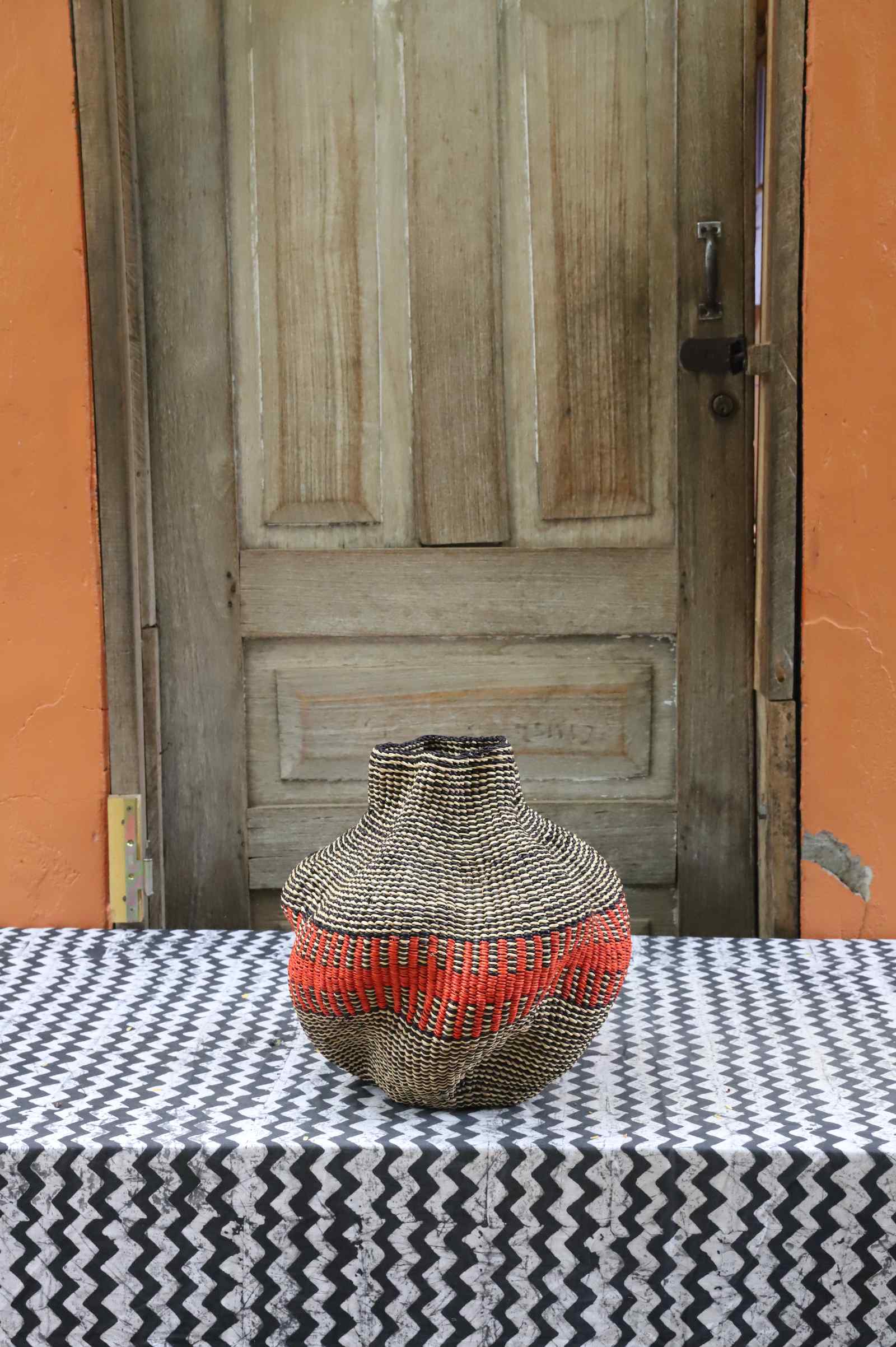Handwoven Bolga art basket in a rounded pot shape, natural straw with a single bold red band.