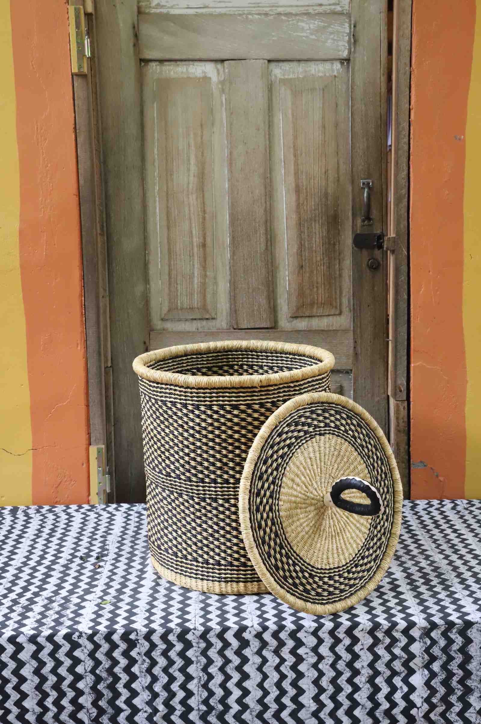 Coiled-rim laundry basket in a black and tan speckled weave, lid resting alongside on a chevron cloth.