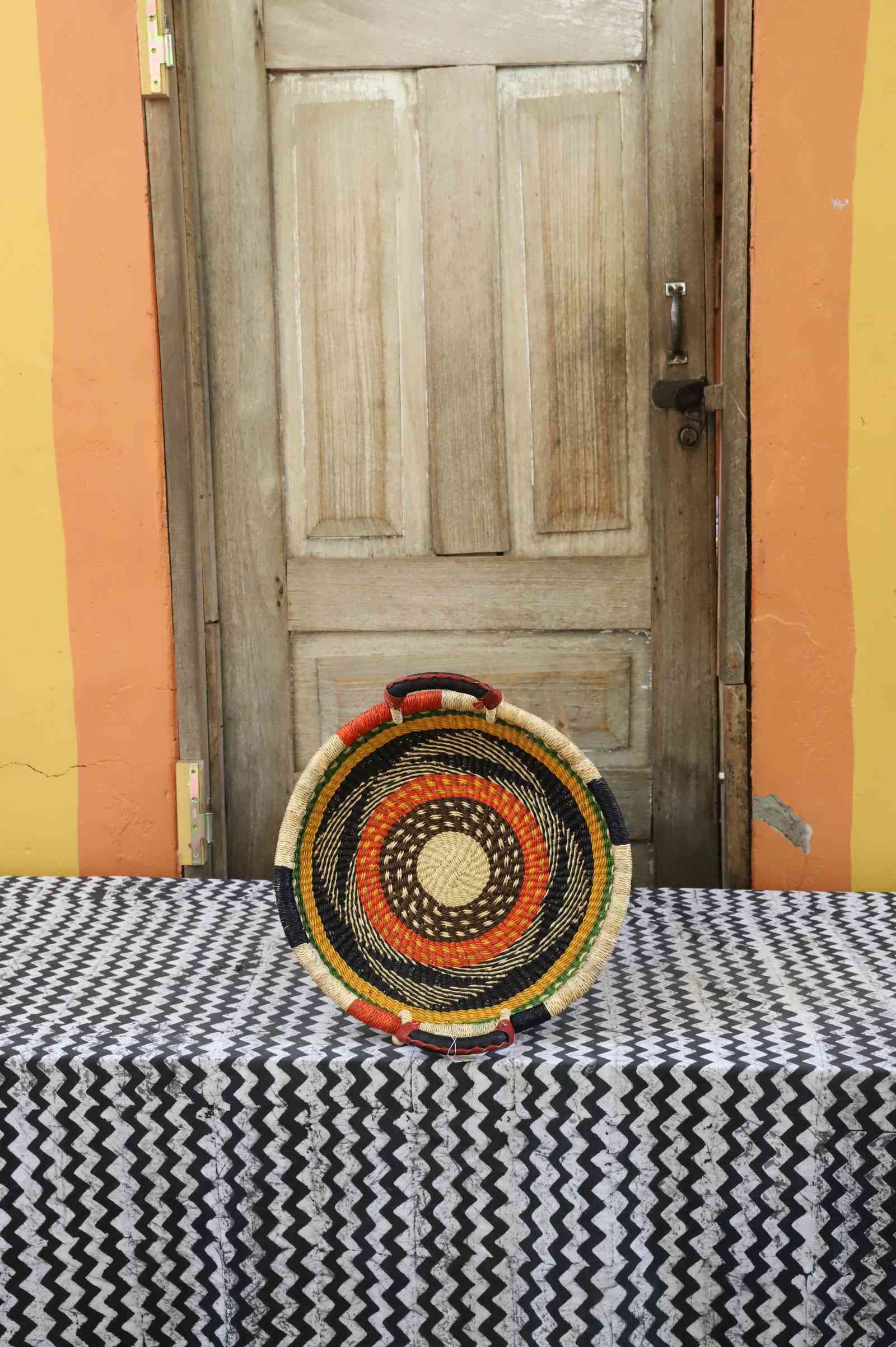 Handwoven Bolga wall tray disc with natural rim, orange and black concentric bands and yellow centre.
