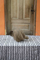 Small spiral-form Bolga art basket in natural straw, side view on a chevron cloth by a wooden door.