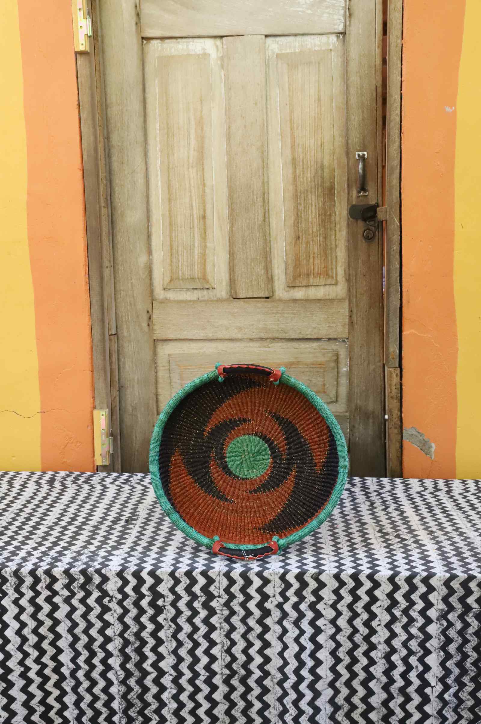 Handwoven Bolga wall tray disc with green rim, orange concentric bands and green centre.