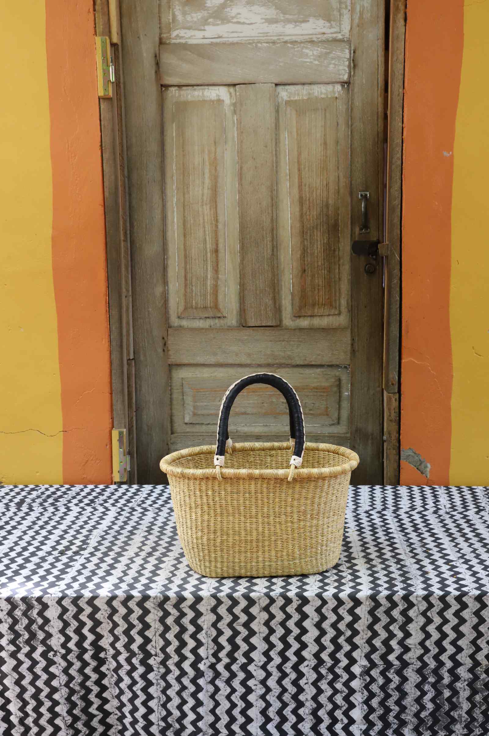 Medium handwoven Bolga Zaane Tia market basket in plain natural straw with a dark leather-wrapped handle.