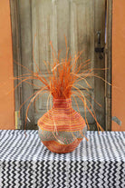 Handwoven Bolga Baobab-inspired basket in dyed orange straw with orange grass sprigs bursting from the top.