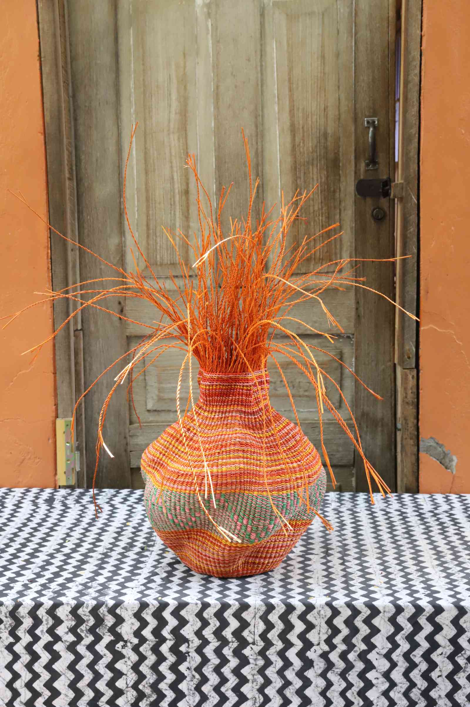 Handwoven Bolga Baobab-inspired basket in dyed orange straw with orange grass sprigs bursting from the top.
