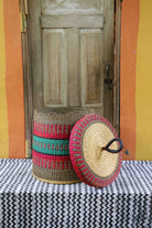 Handwoven Bolga laundry basket with lid removed, showing red and green banded body and natural woven lid.