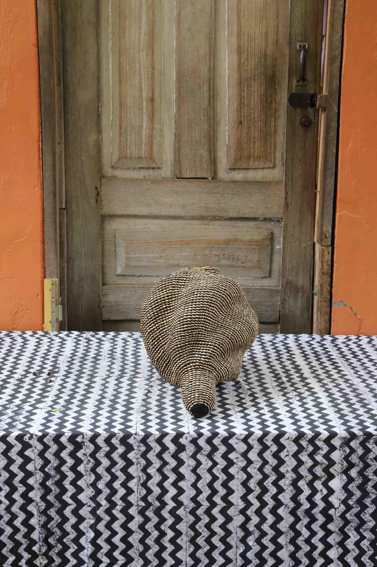 Small spiral-form Bolga art basket in natural straw, rear view on a chevron cloth.