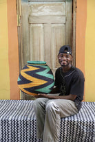 Handwoven African art basket with bold diagonal zigzag pattern in teal, black and amber, held by a man in Bolgatanga.