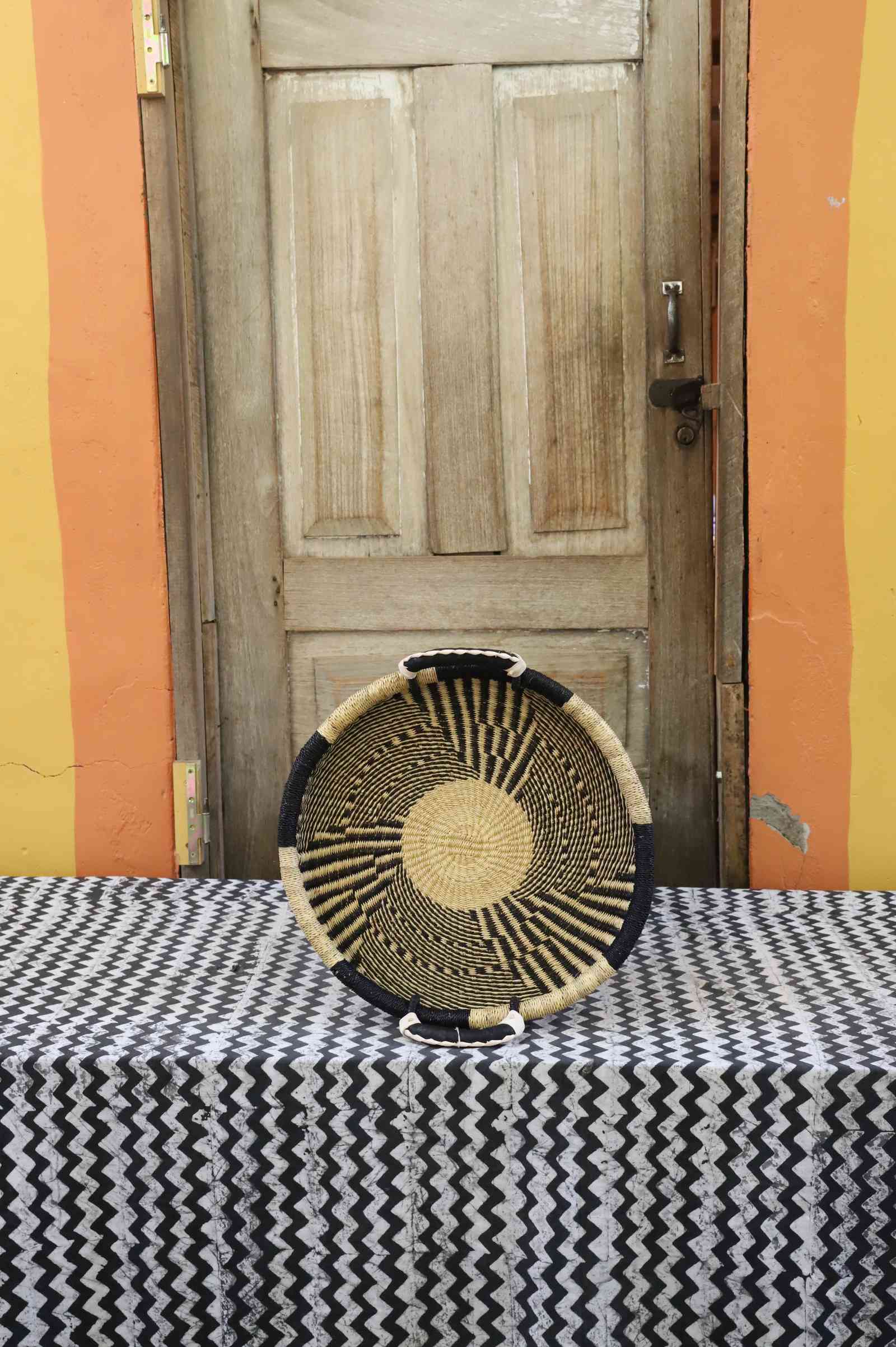 Handwoven Bolga wall tray disc in dark straw with fine radial stripes and a natural centre.