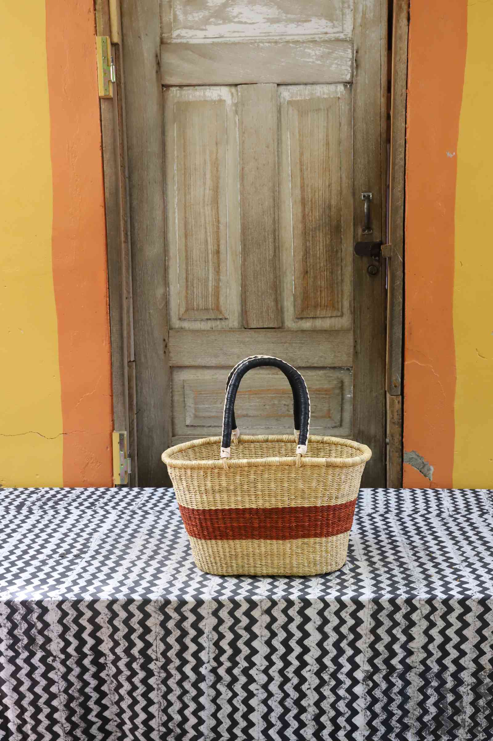 Medium handwoven Bolga Zaane Tia market basket in natural straw with a rust-orange band and leather handle.