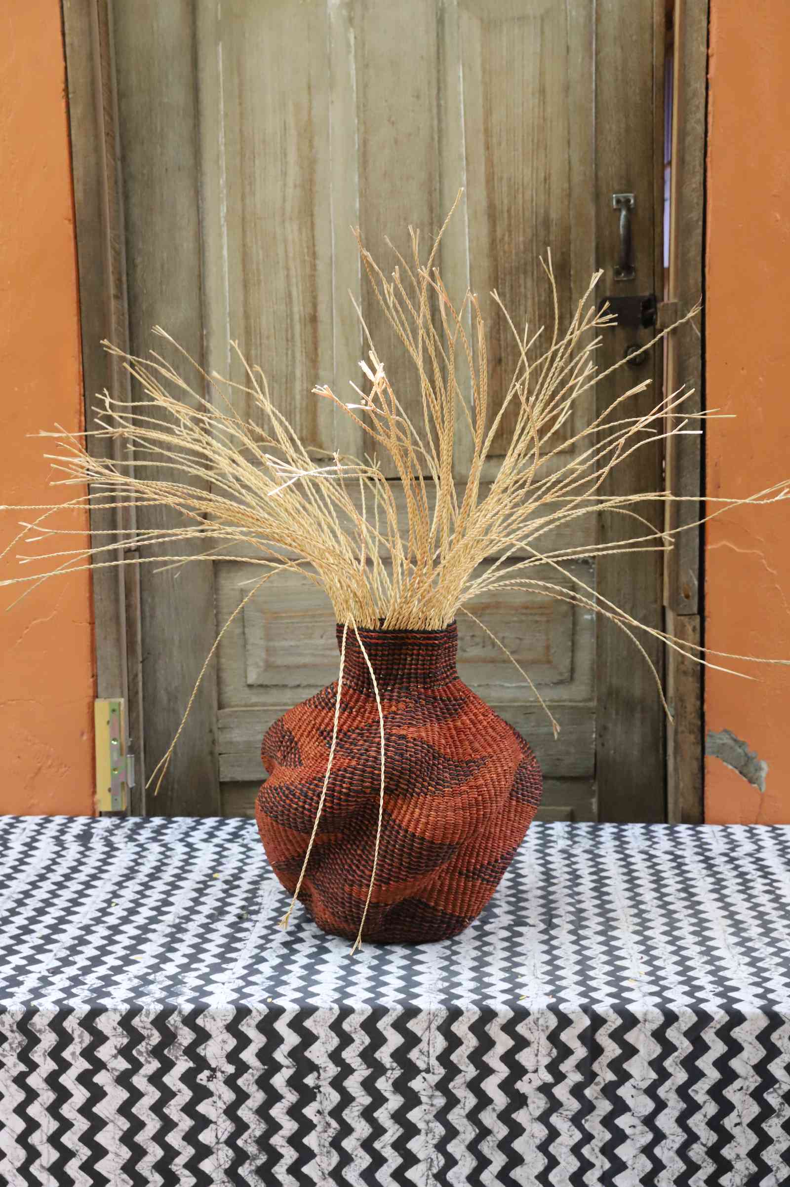 Handwoven Bolga Baobab-inspired basket in dyed rust-red with a fine diamond weave and cream grass sprigs.
