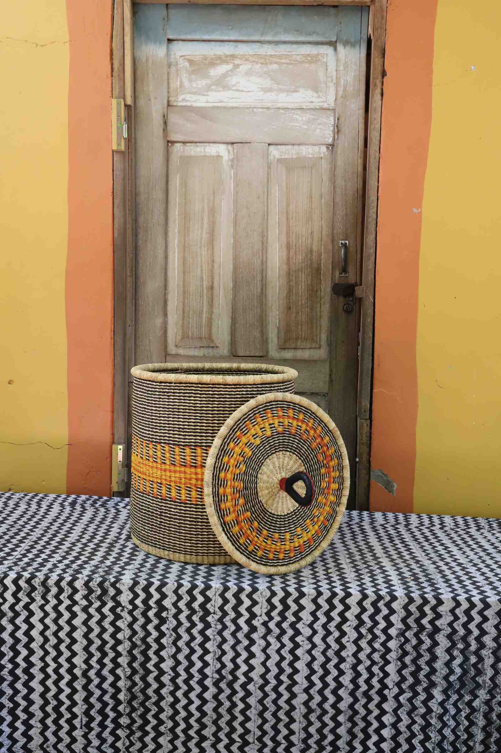 Handwoven Bolga laundry basket with lid removed, natural body with orange band and multicolour rim lid.