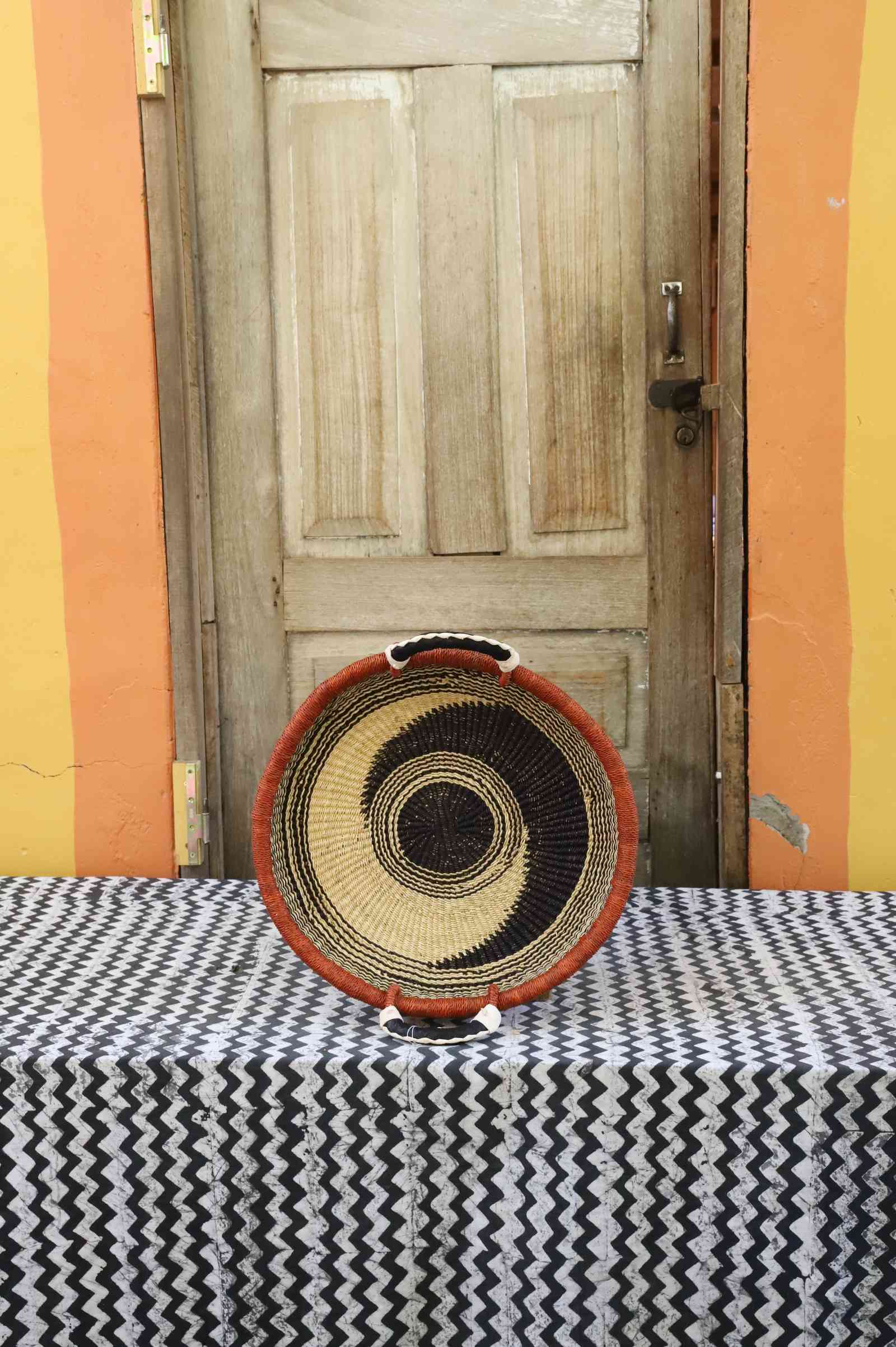 Handwoven Bolga wall tray disc with orange rim, black concentric rings and natural centre.