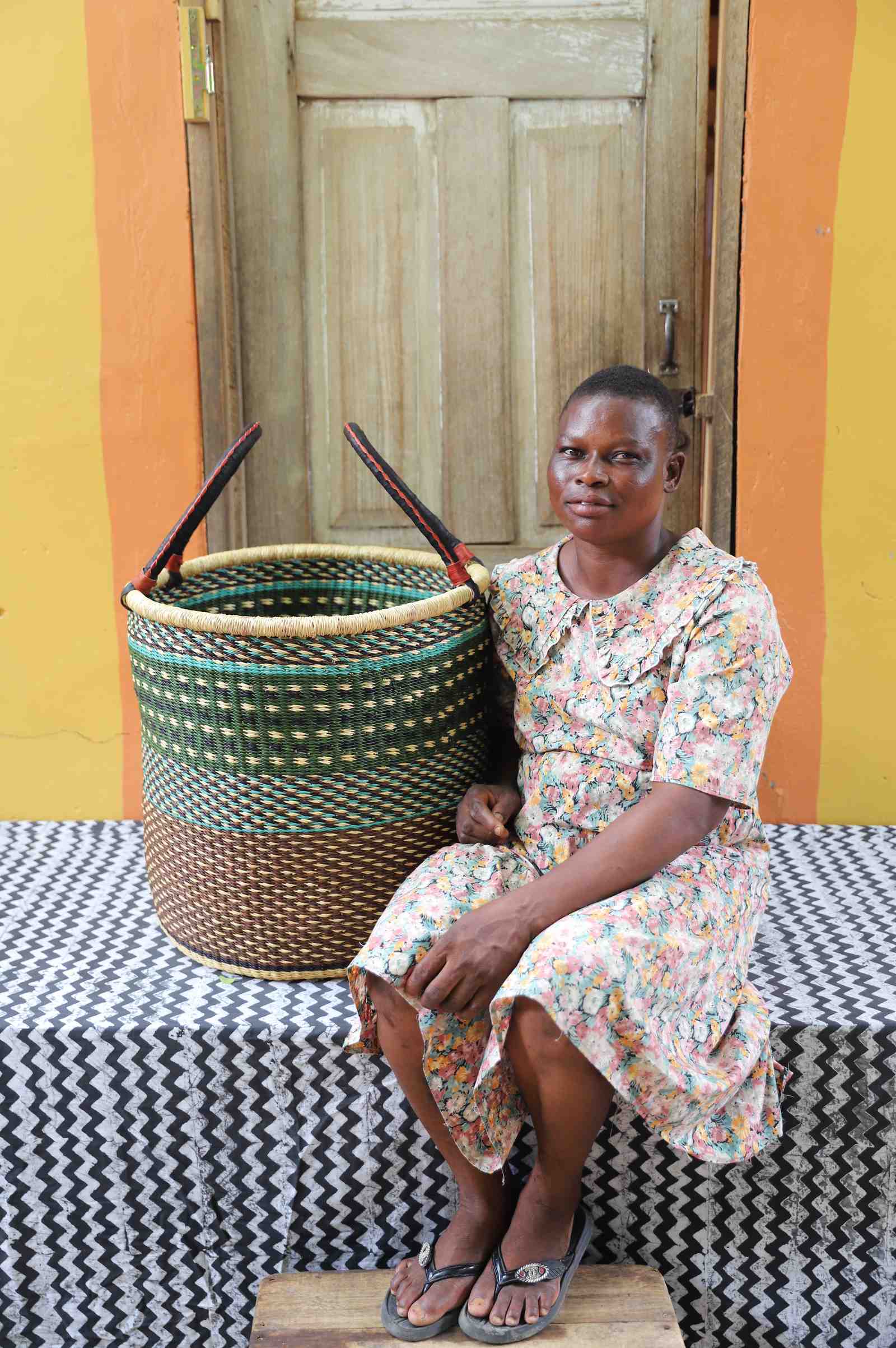 Large open laundry basket in green checkered weave with a dark brown base, held by a seated person for scale.