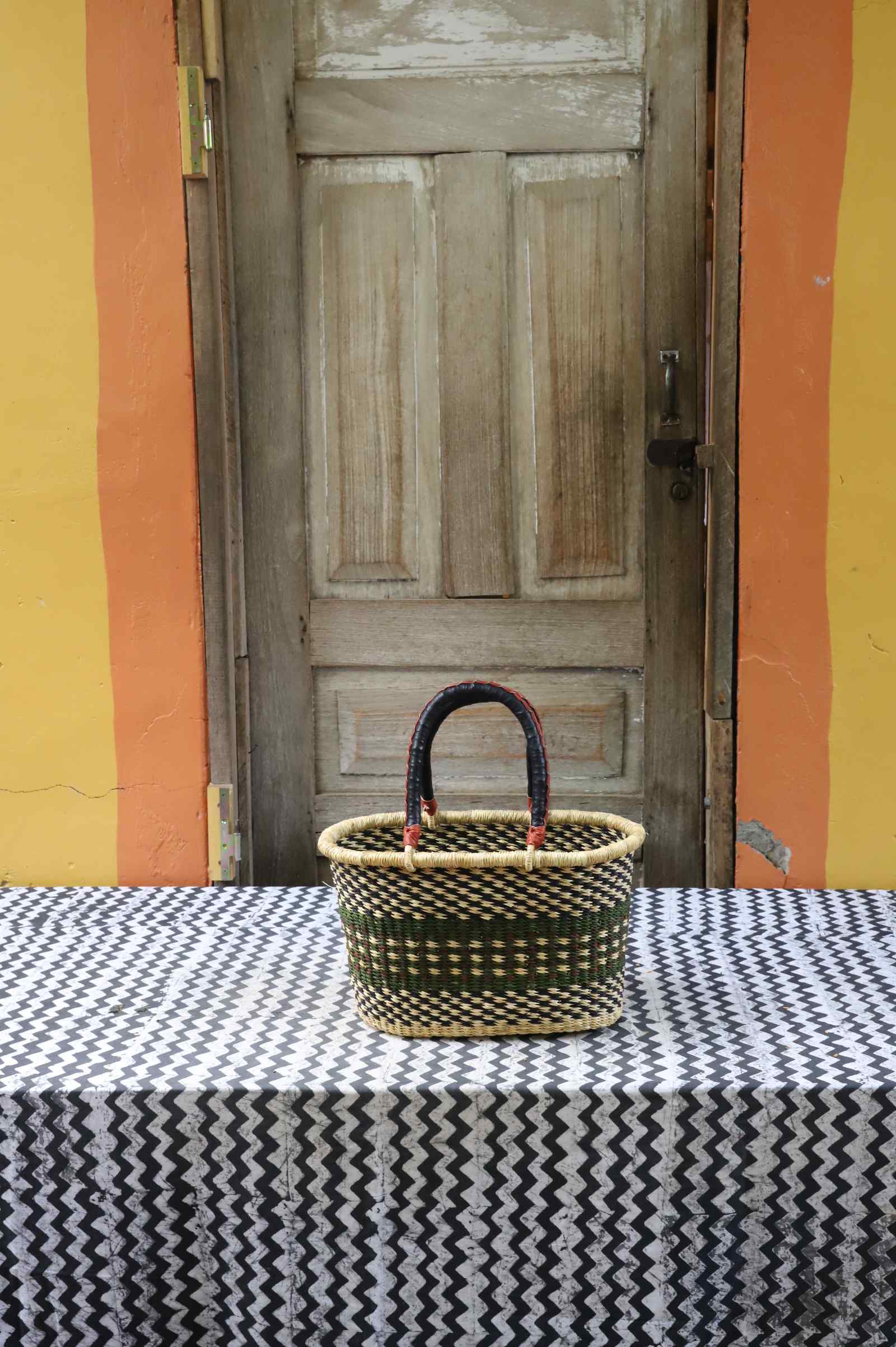 Small handwoven Bolga Zaane Tia market basket in natural straw with a dark and orange zigzag weave band.