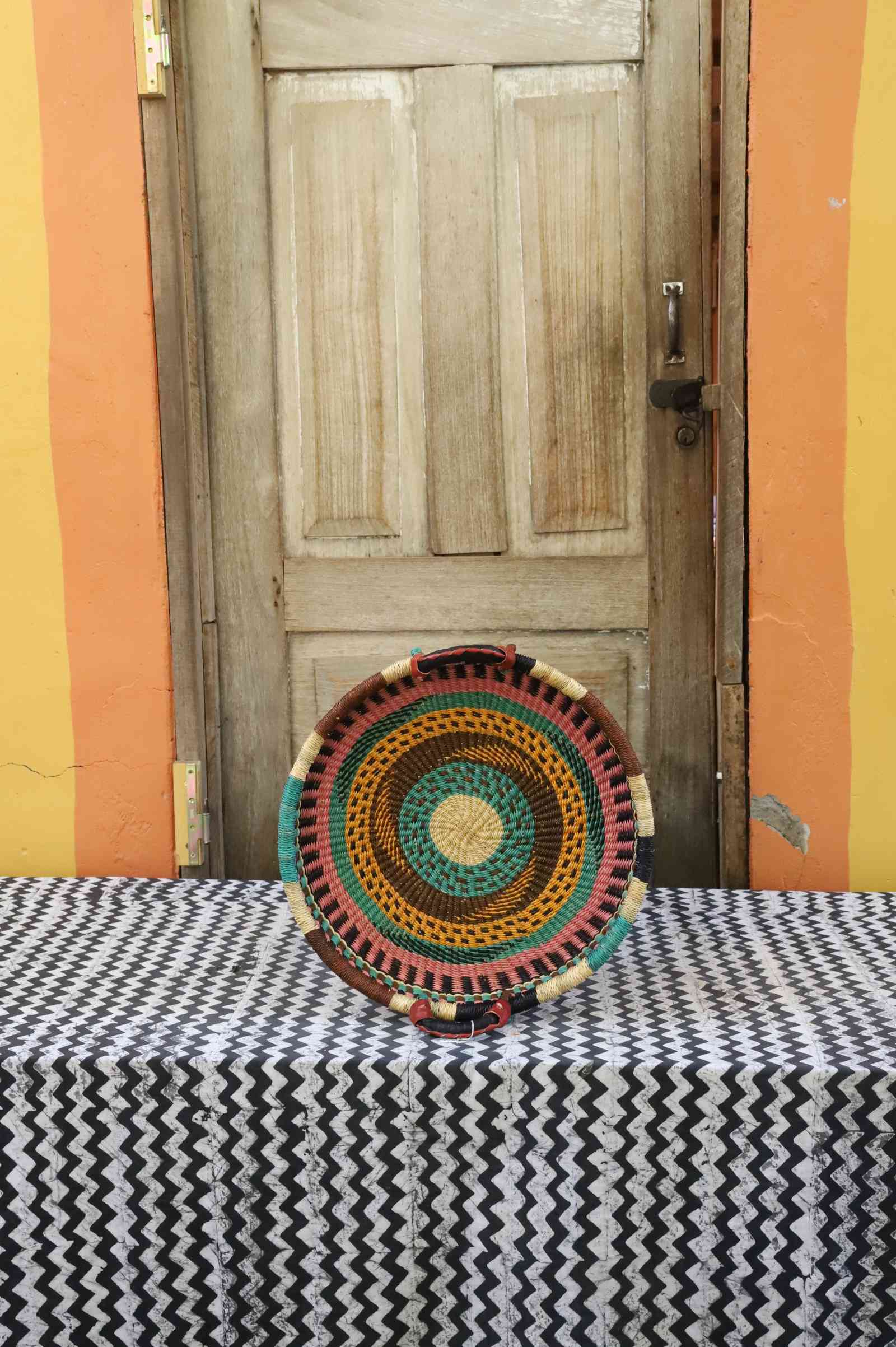 Handwoven Bolga wall tray disc with natural rim, red and green concentric bands and yellow centre.