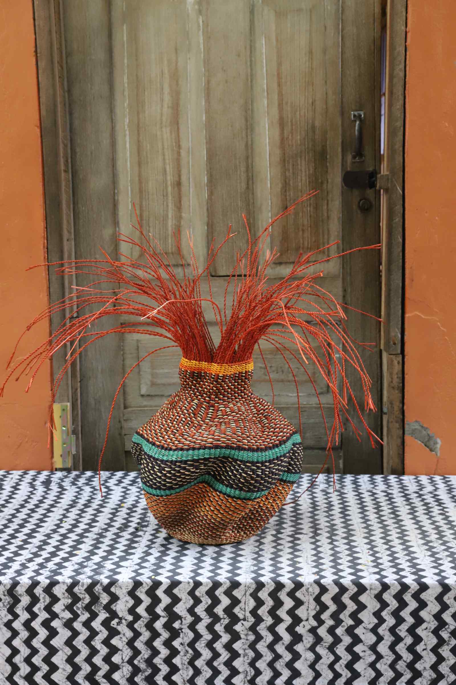 Handwoven Bolga Baobab-inspired basket in natural straw with teal and black scalloped bands and orange grass sprigs.