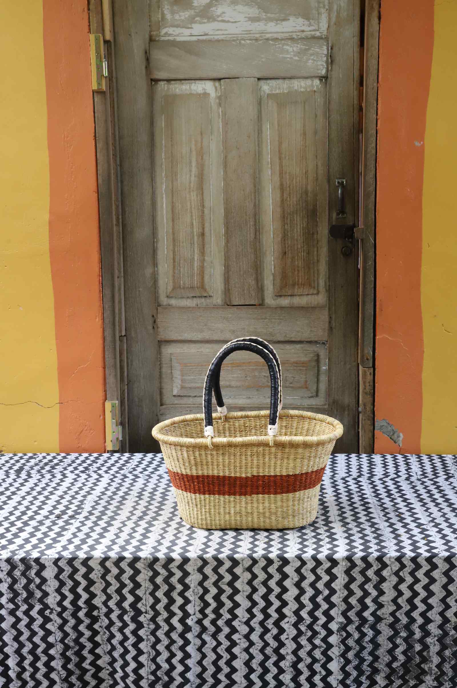 Small handwoven Bolga Zaane Tia market basket in natural straw with a rust-orange band and leather-wrapped handle.