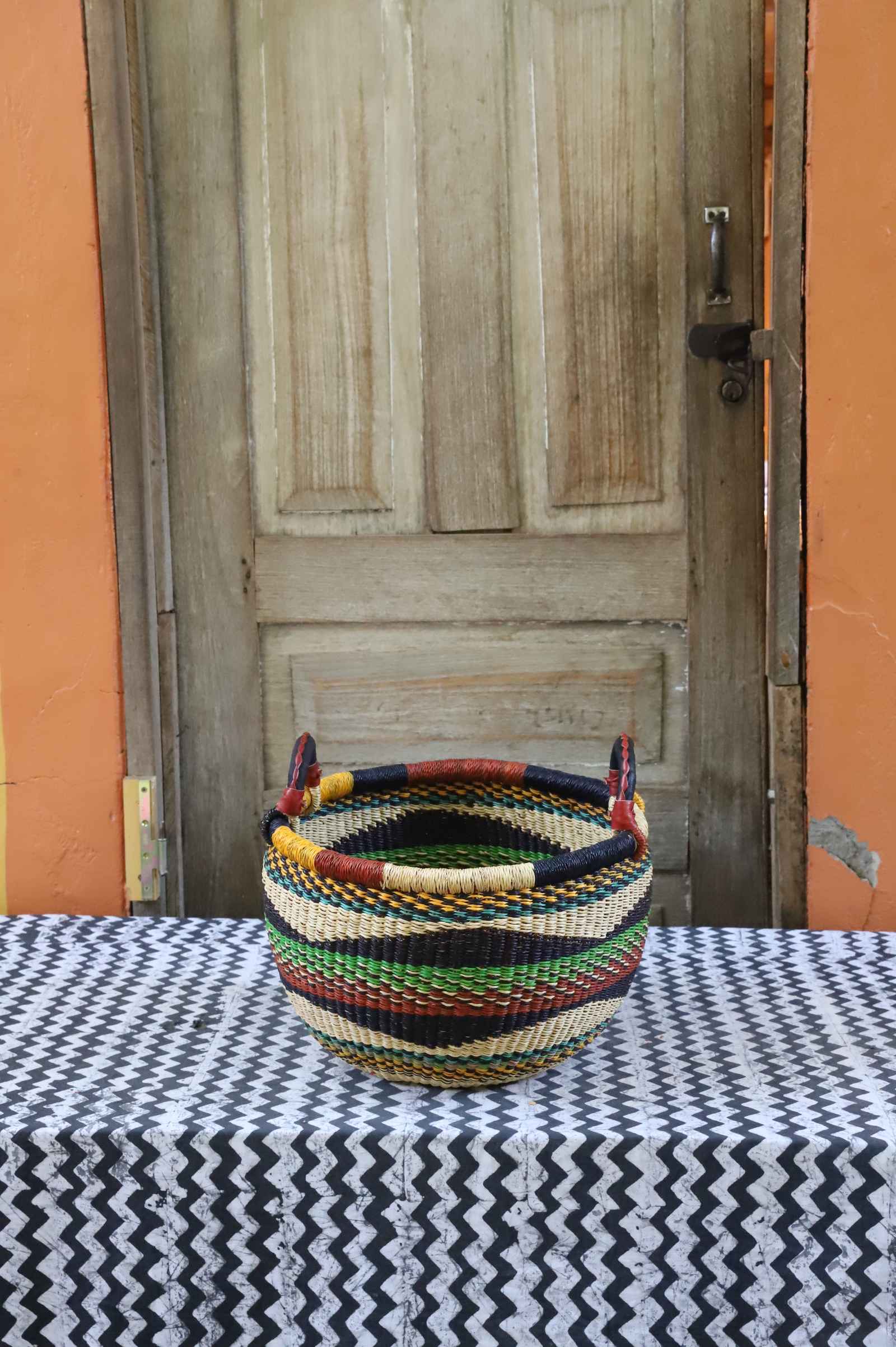 Small handwoven Bolga Gbenka storage basket with green, red, black and yellow banded stripes.