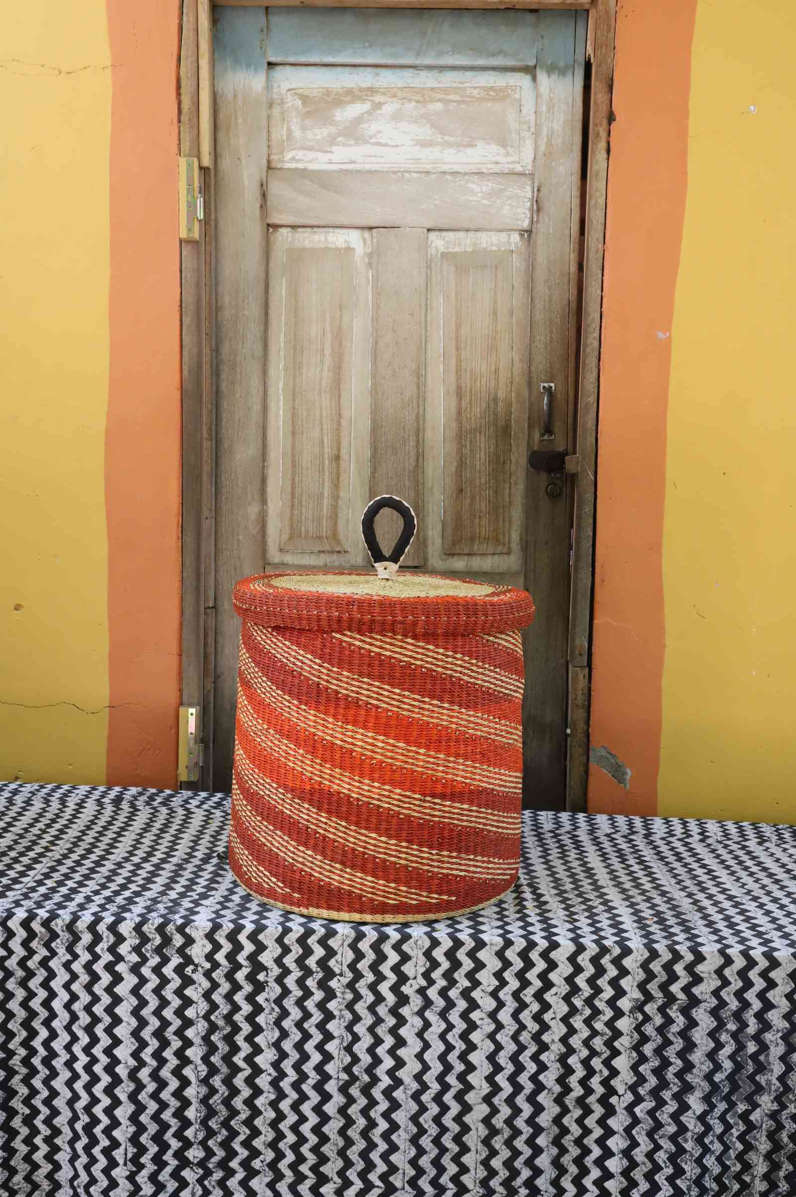 Handwoven Bolga laundry basket with lid dyed bold rust-orange with fine wavy stripes.
