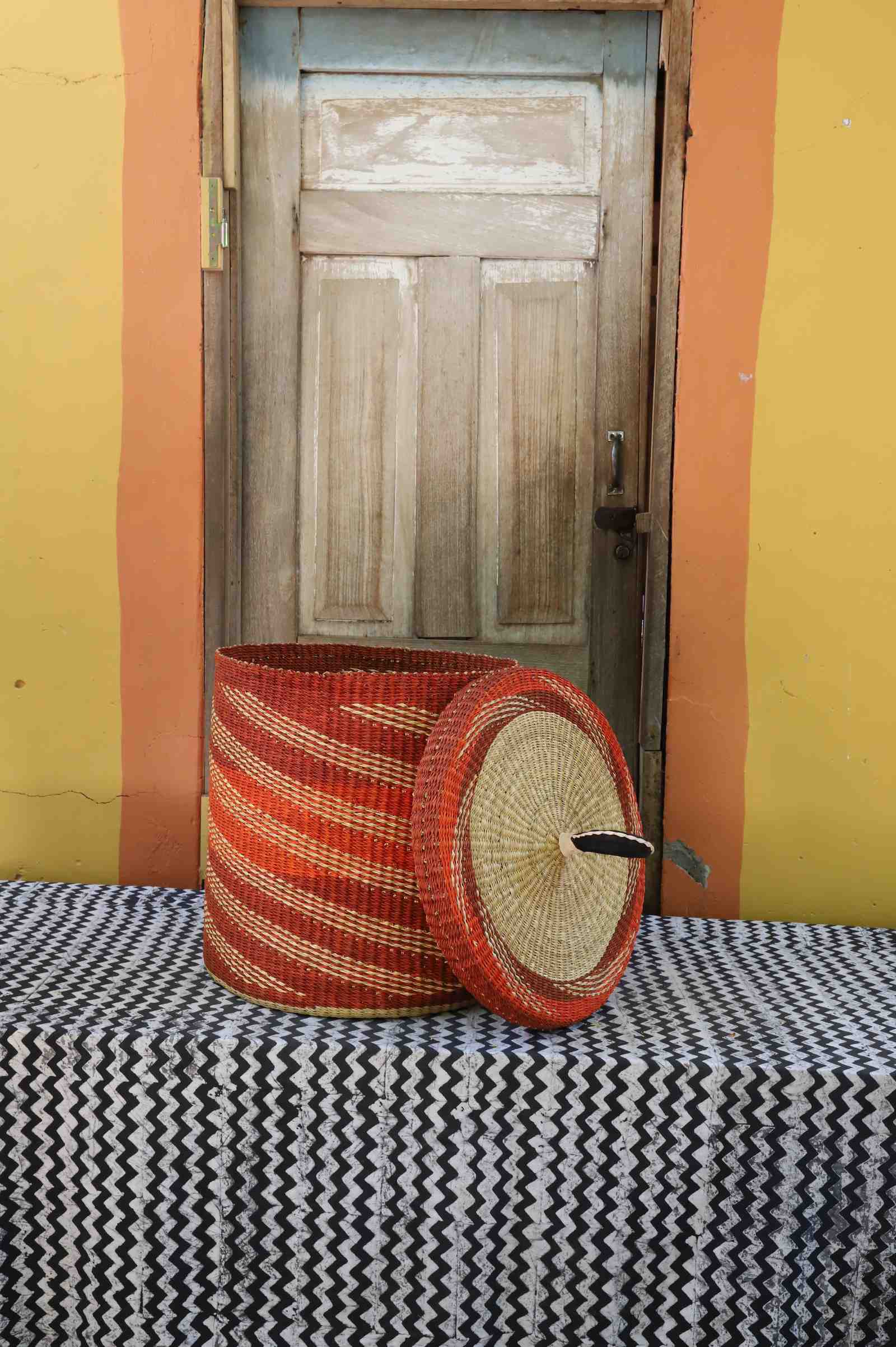 Handwoven Bolga laundry basket with lid removed, rust-orange body with fine wavy stripes and matching lid.