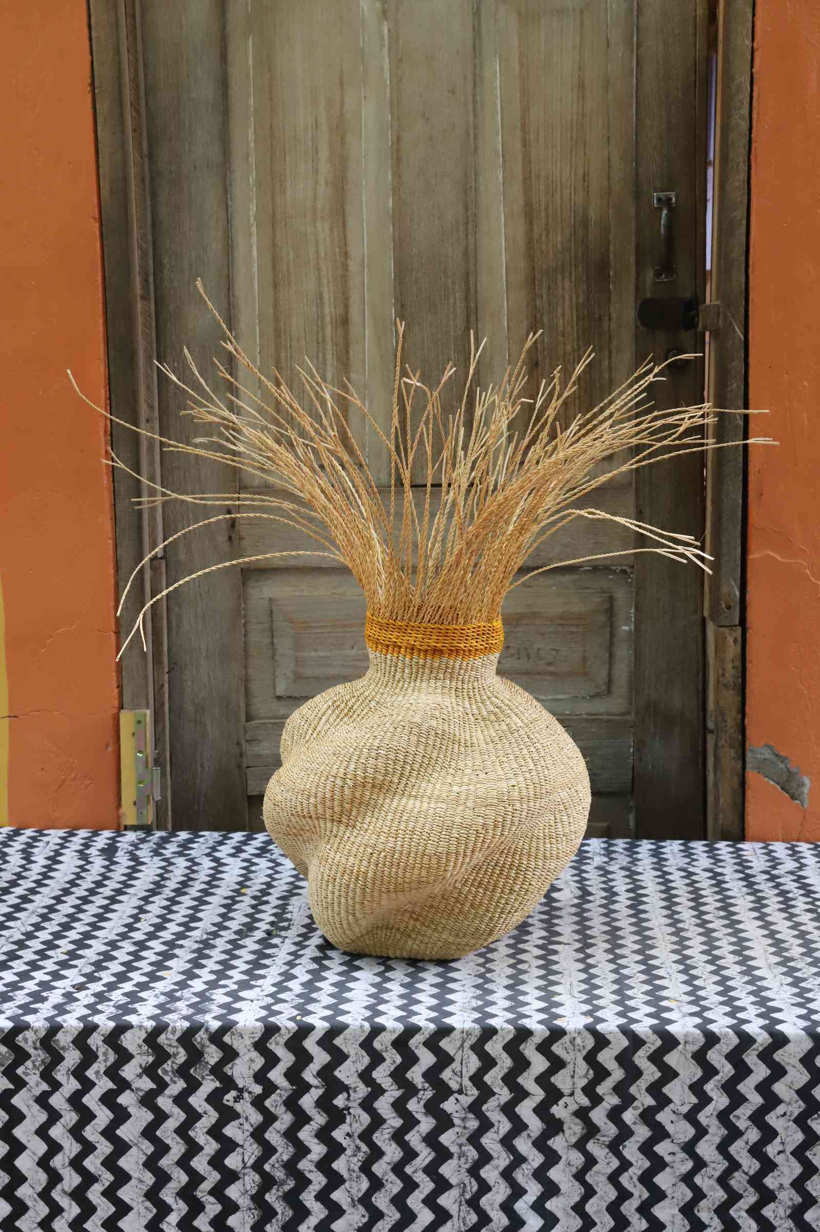 Handwoven Bolga Baobab-inspired basket in all natural straw with natural grass sprigs bursting from the top.