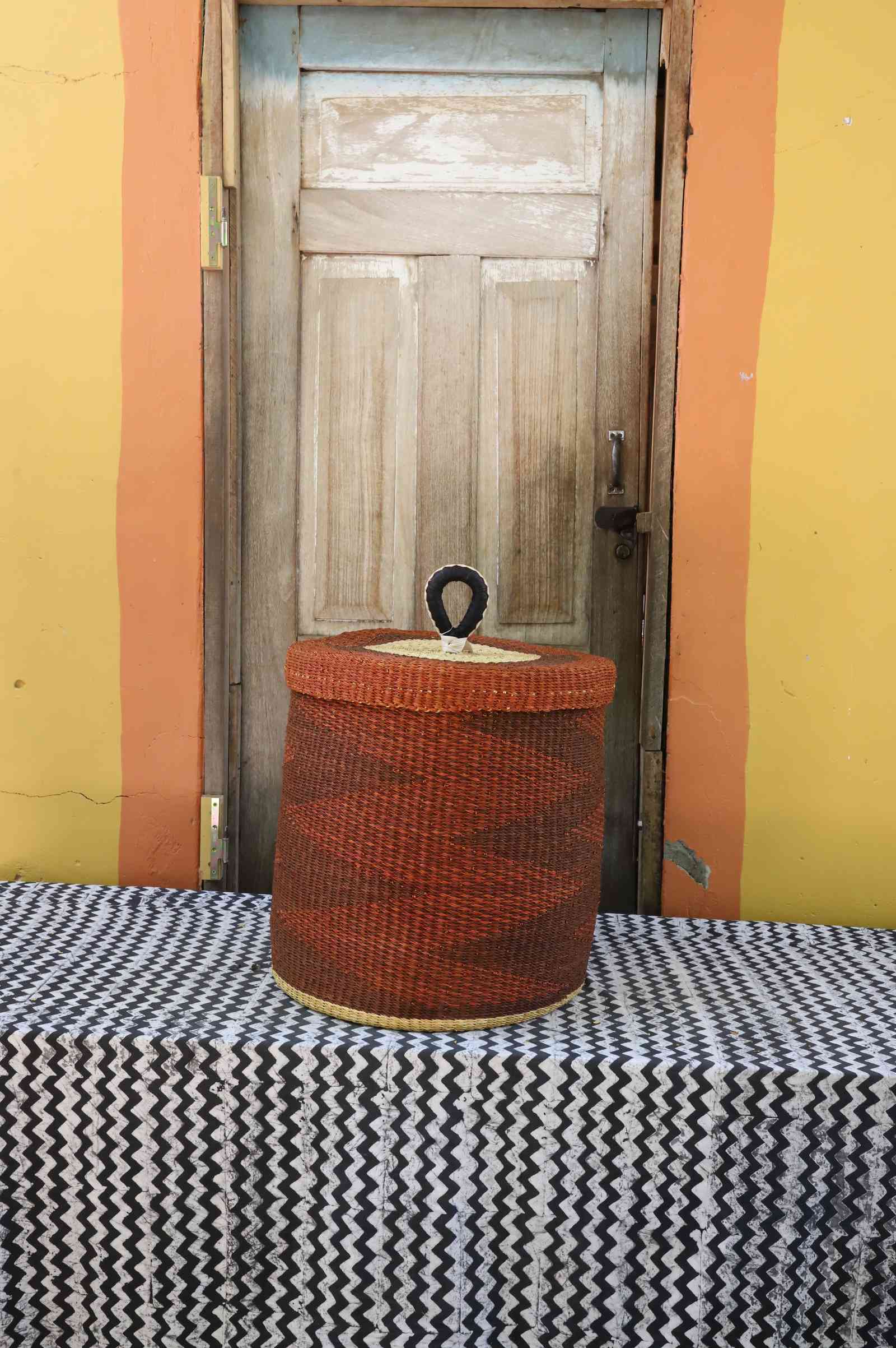 Handwoven Bolga laundry basket with lid dyed rust-red with a natural rim highlight.
