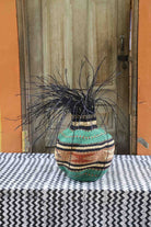 Handwoven Bolga Baobab-inspired basket in natural straw with teal and dark green bands and black grass sprigs.