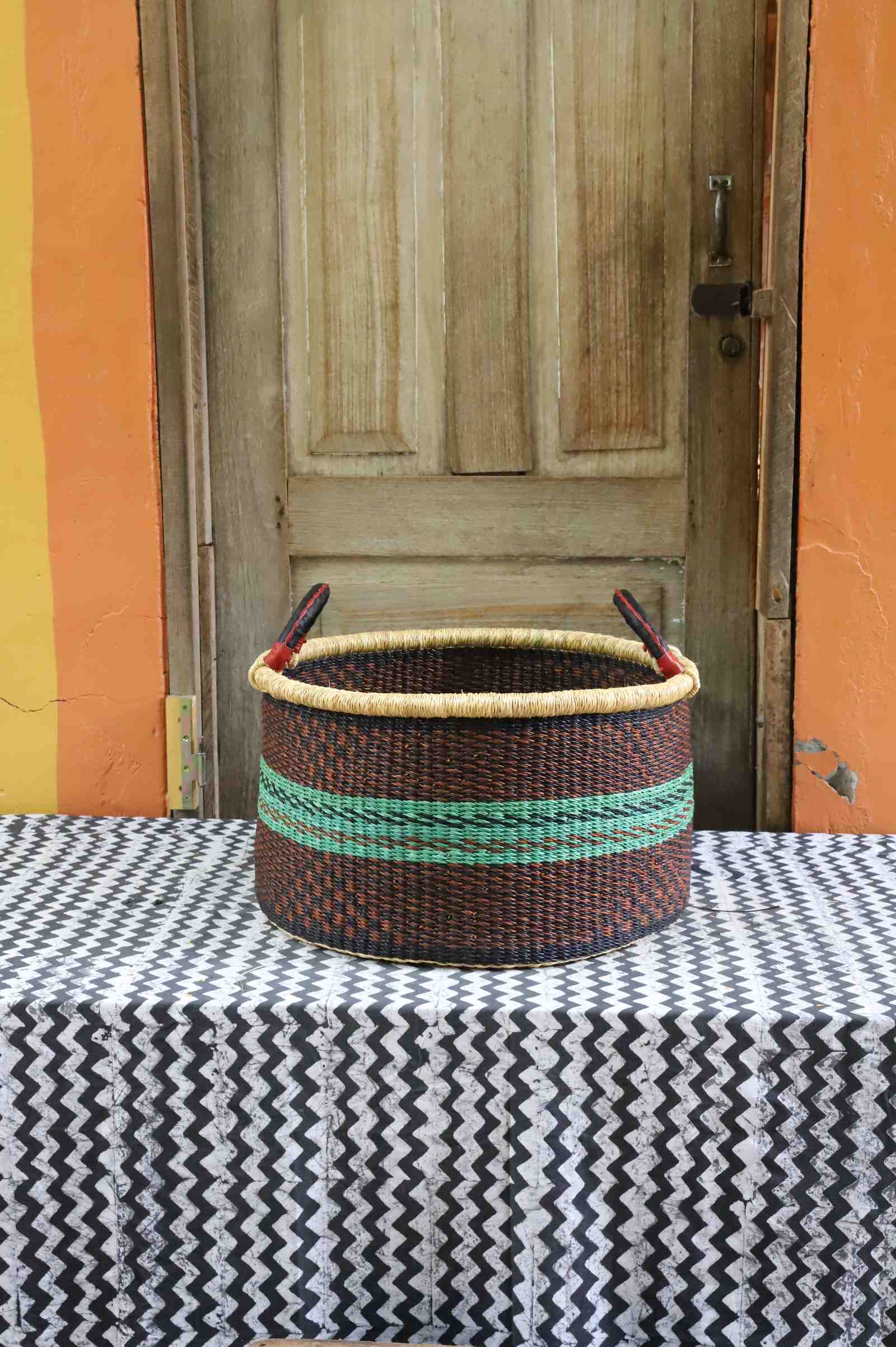Handwoven Bolga storage basket in dark brown with green horizontal stripes and twin leather-wrapped handles.