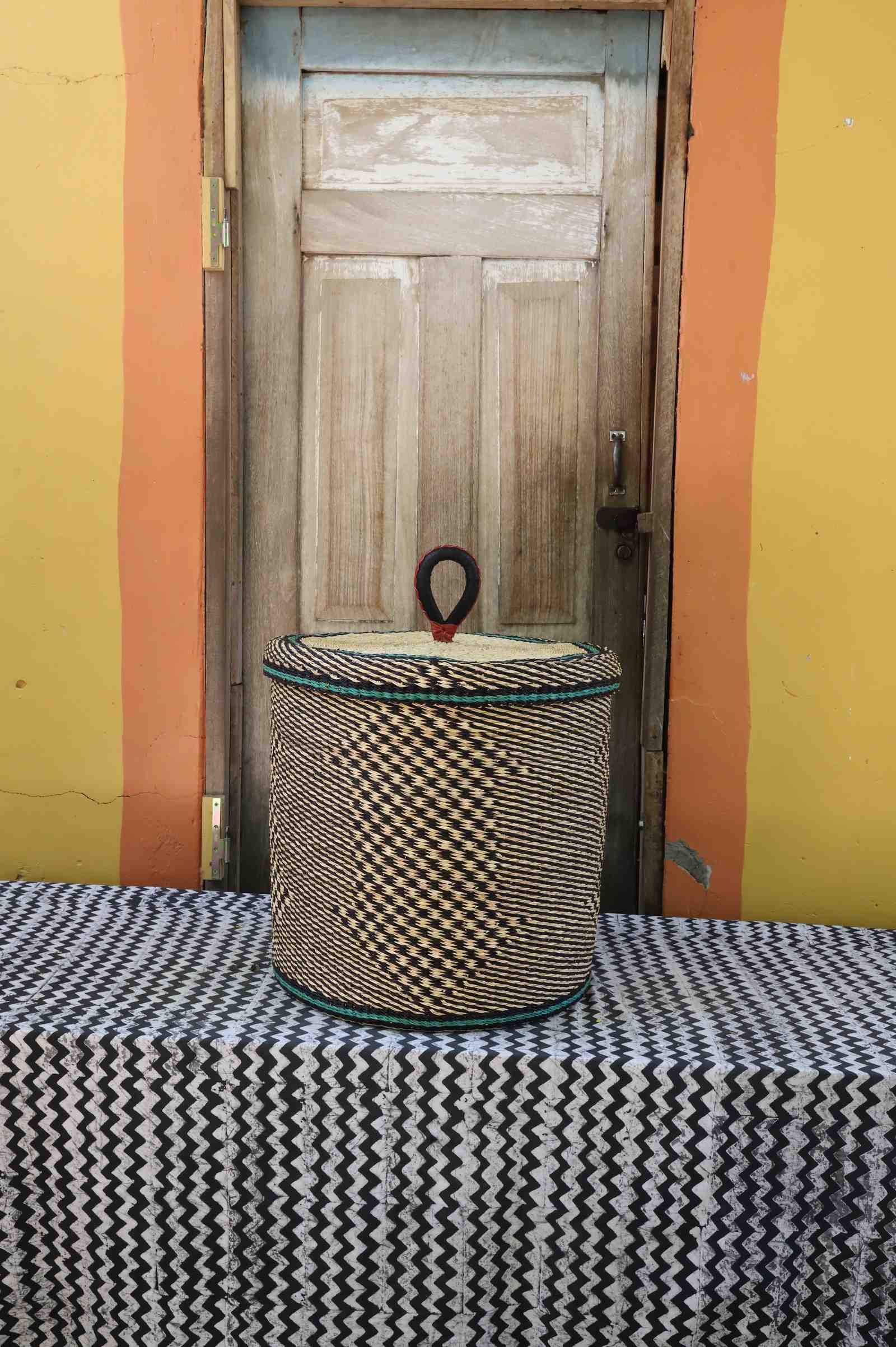 Handwoven Bolga laundry basket with lid in natural straw with a black checkerboard pattern.