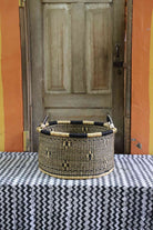 Handwoven Bolga storage basket in natural straw with a subtle dark motif and black-and-cream banded rim.