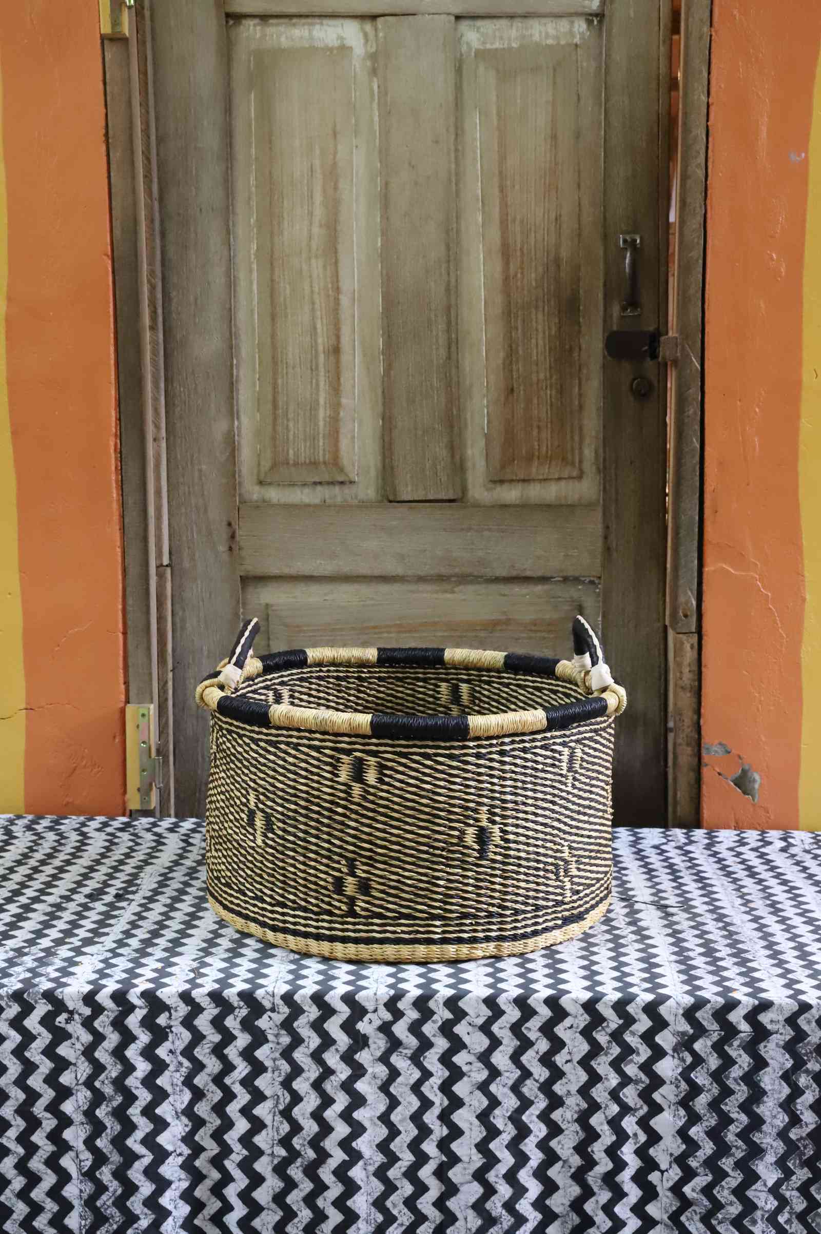 Handwoven Bolga storage basket in natural straw with a subtle dark motif and black-and-cream banded rim.