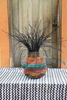Handwoven Bolga Baobab-inspired basket in natural straw with pink, teal and yellow bands and dark grass sprigs.