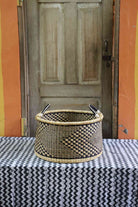 Handwoven Bolga storage basket in natural straw with a dark geometric weave and twin leather-wrapped handles.