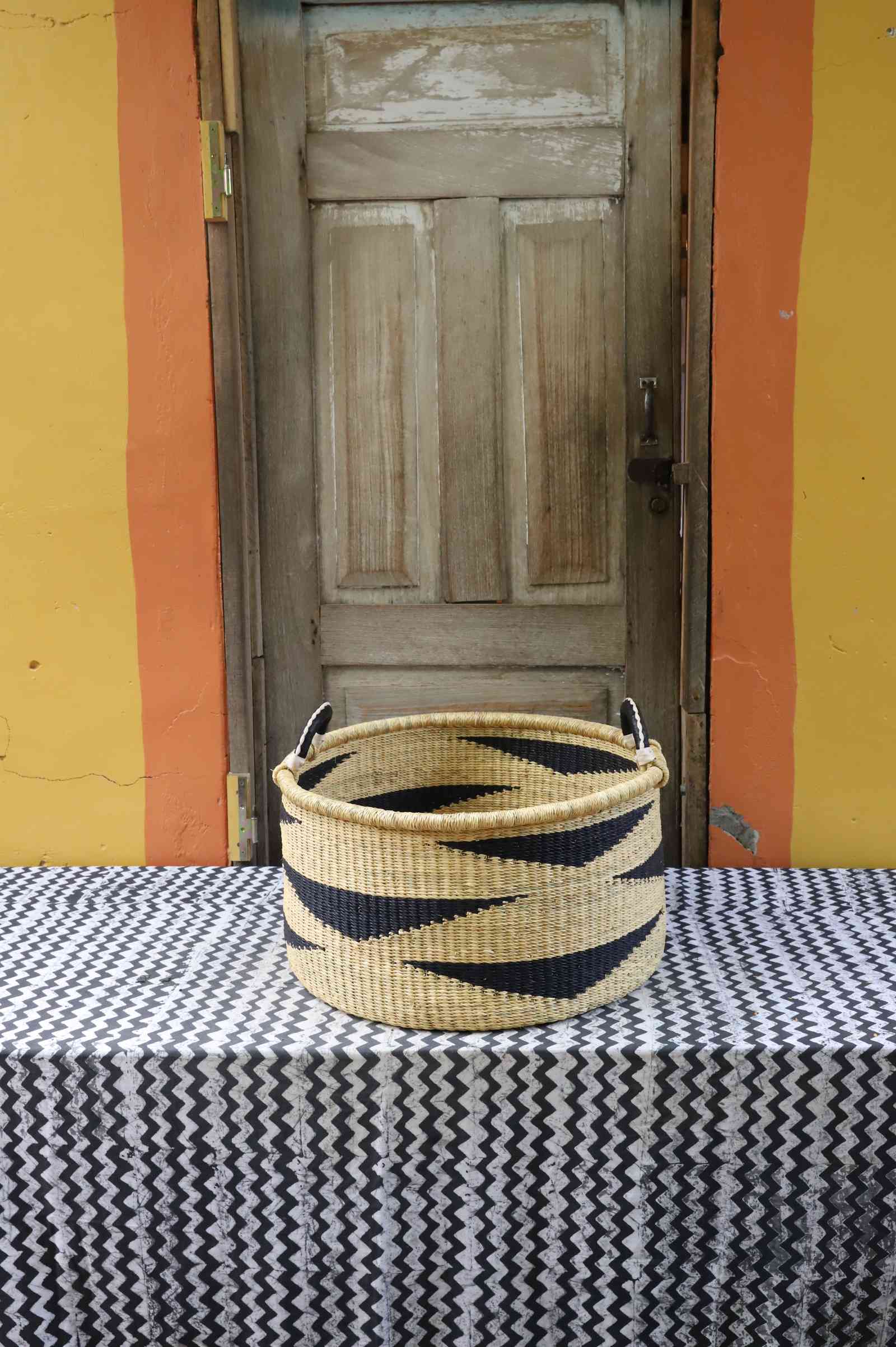 Large handwoven Bolga storage tub in dyed bold orange with a plain woven body and leather-wrapped handles.