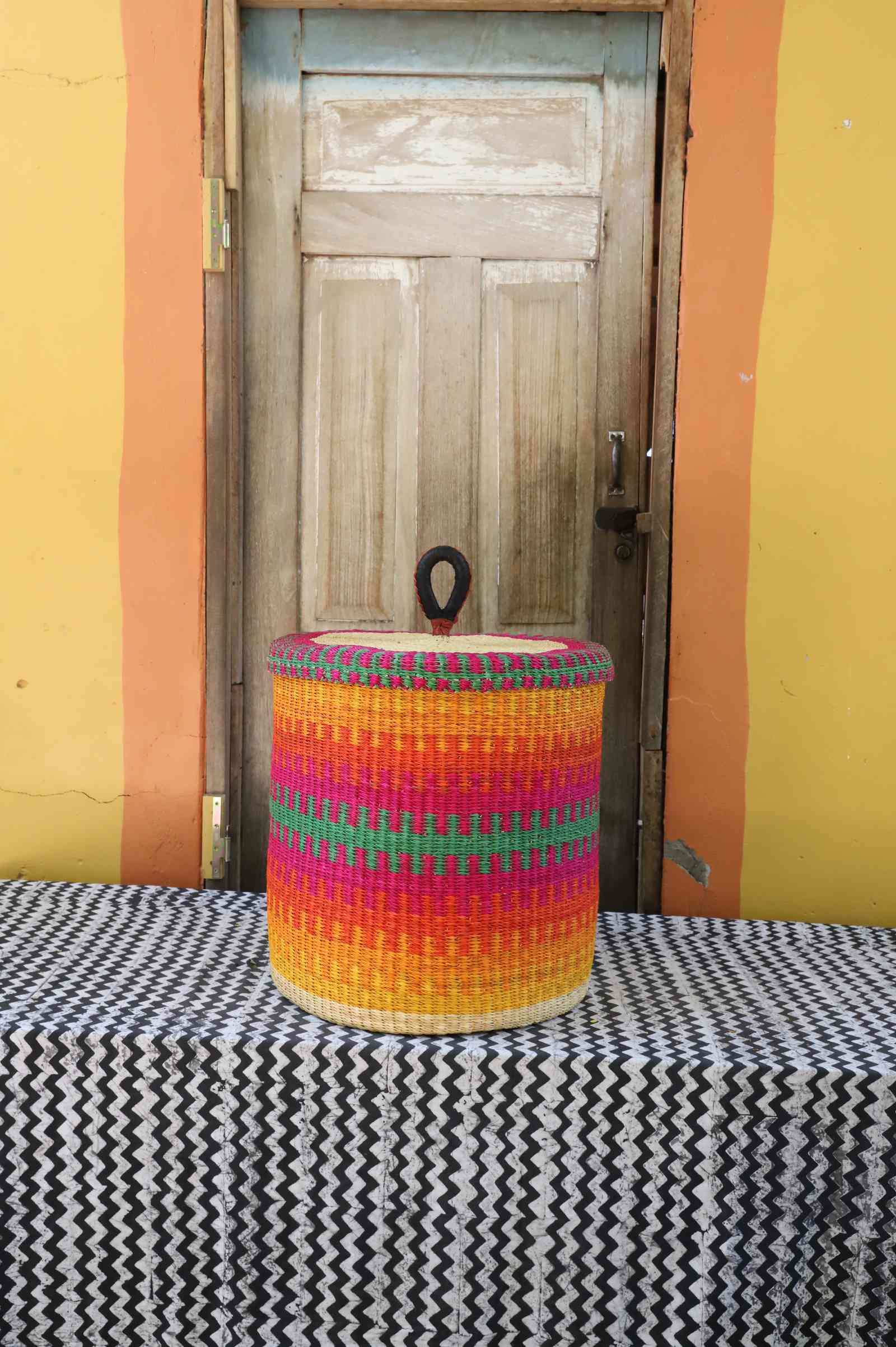 Handwoven Bolga laundry basket with lid in fine multicolour stripes of pink, orange, yellow and green.
