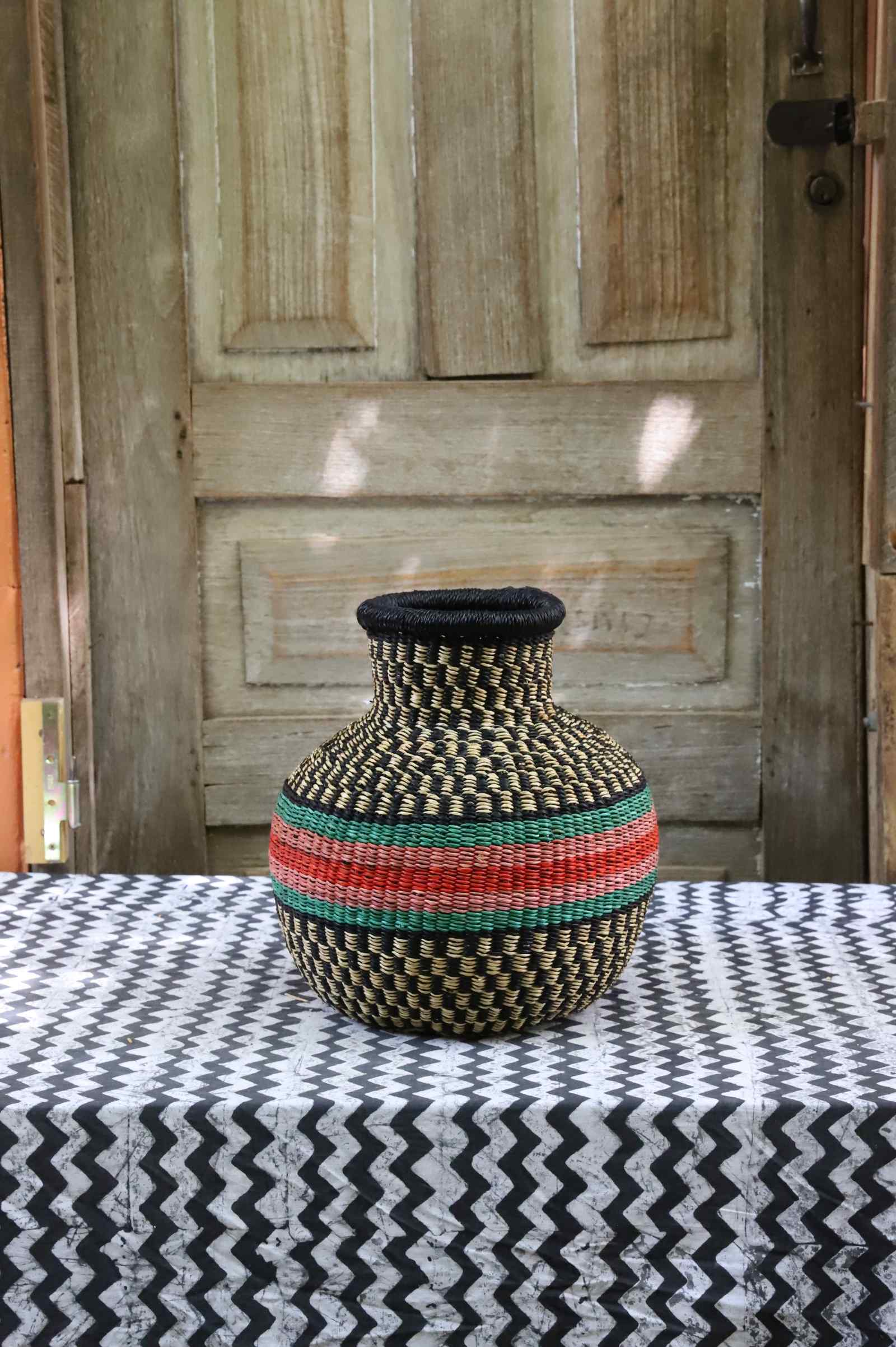 Small vase-shaped Bolga basket in black and cream weave with a red and green striped band, on a tablecloth.