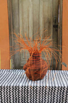 Handwoven Bolga Baobab-inspired basket in dyed orange straw with a plain body and orange grass sprigs.