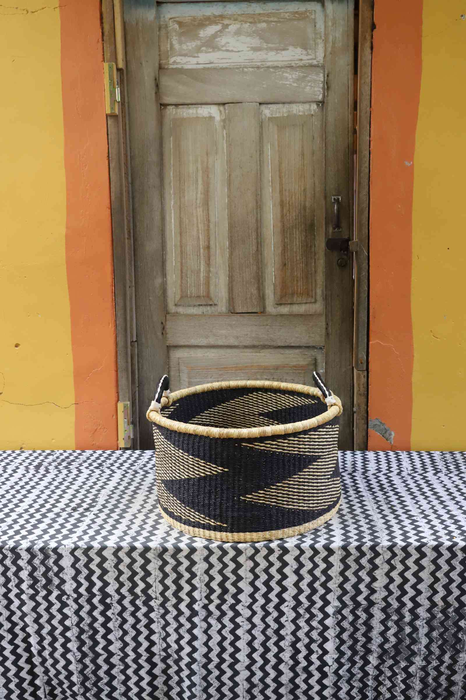 Medium handwoven Bolga storage tub in natural straw with a dark zigzag pattern and leather-wrapped handles.
