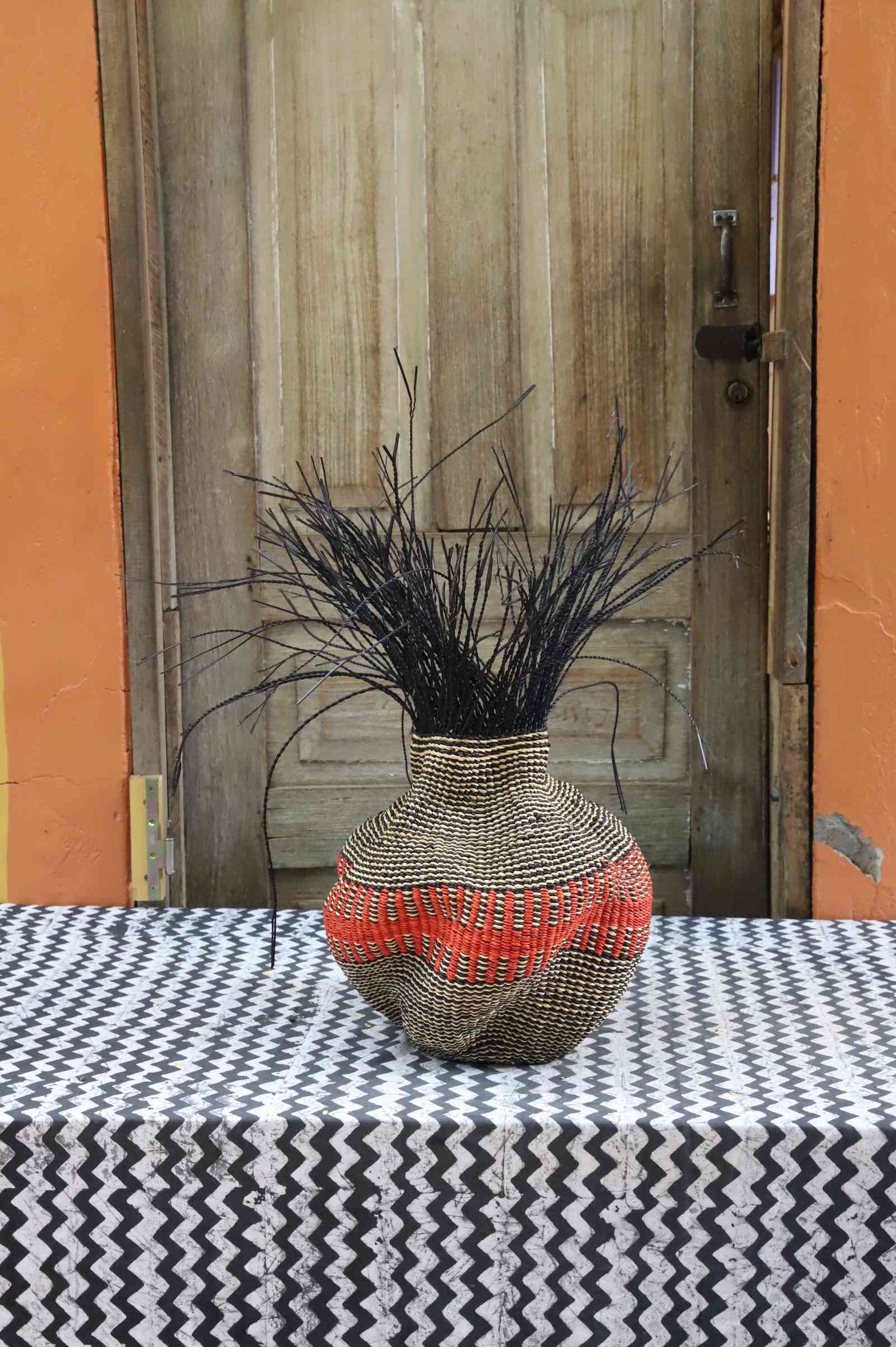Handwoven Bolga Baobab-inspired basket in natural straw with a bold red central band and black grass sprigs.
