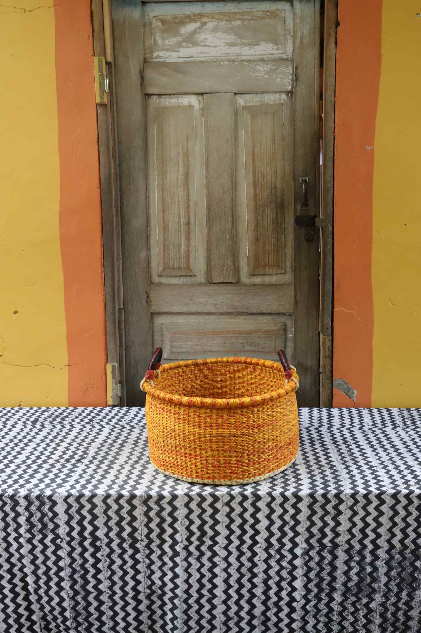 Small handwoven Bolga storage tub in natural straw with dark banded stripes and an orange central band.