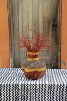Handwoven Bolga Baobab-inspired basket in natural straw with orange banded shoulder and orange grass sprigs on top.