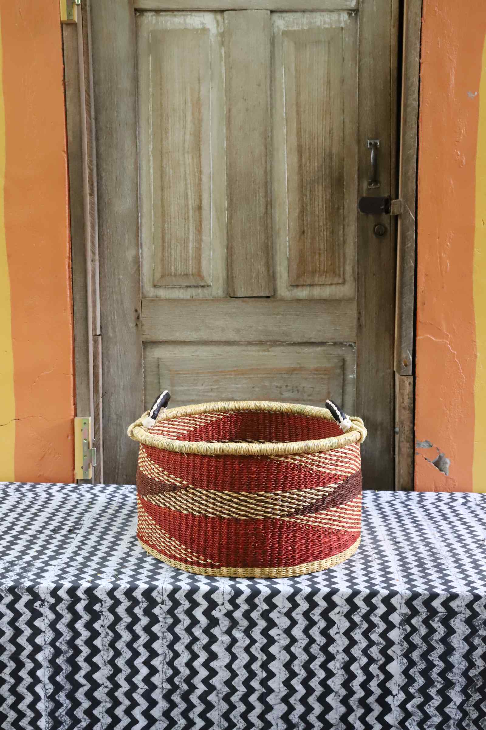 Handwoven Bolga basket in natural straw with red and burgundy geometric stripes and twin leather-wrapped handles.