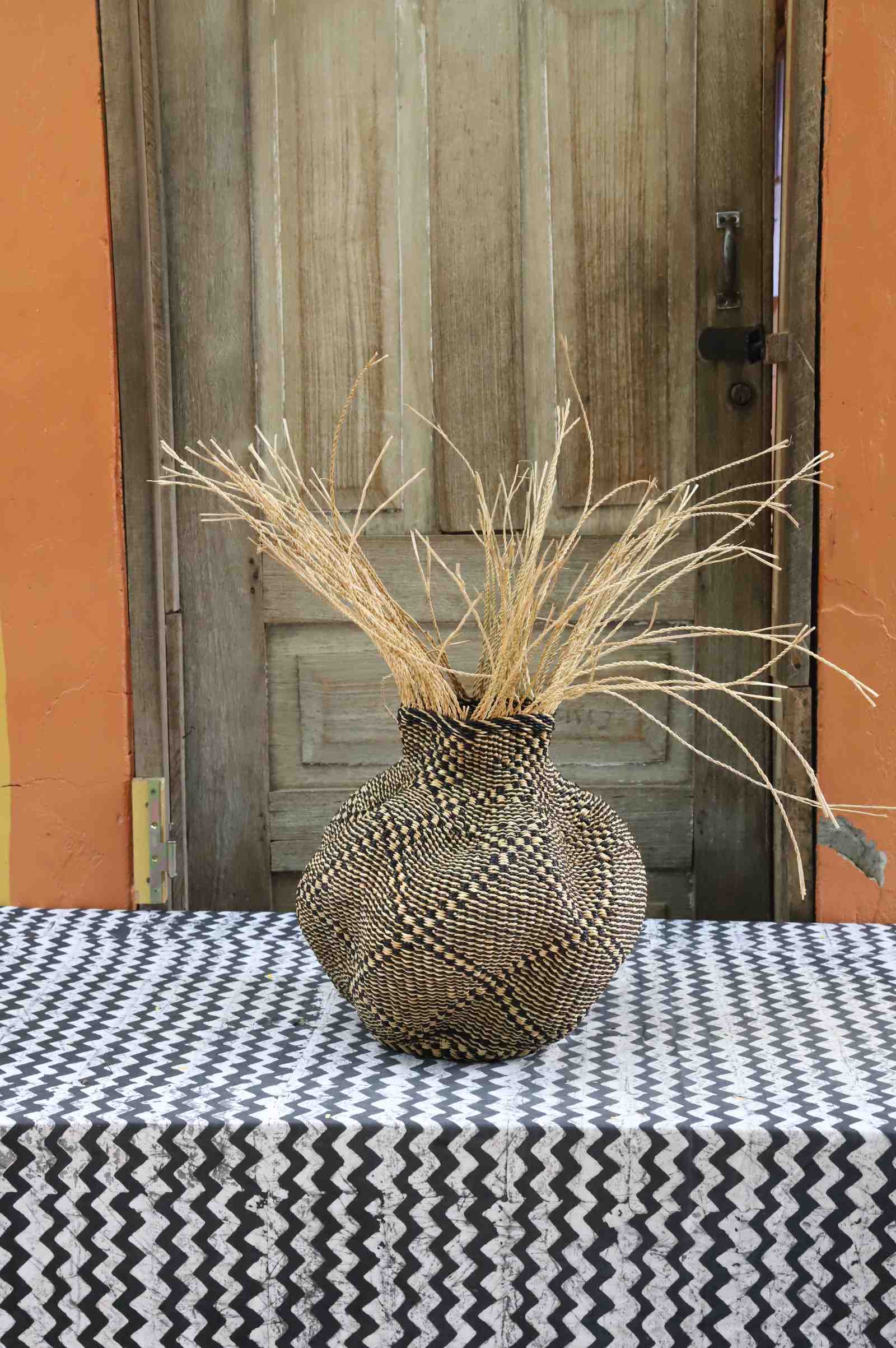 Handwoven Bolga Baobab-inspired basket in natural straw with a fine dark diamond weave and natural grass sprigs.