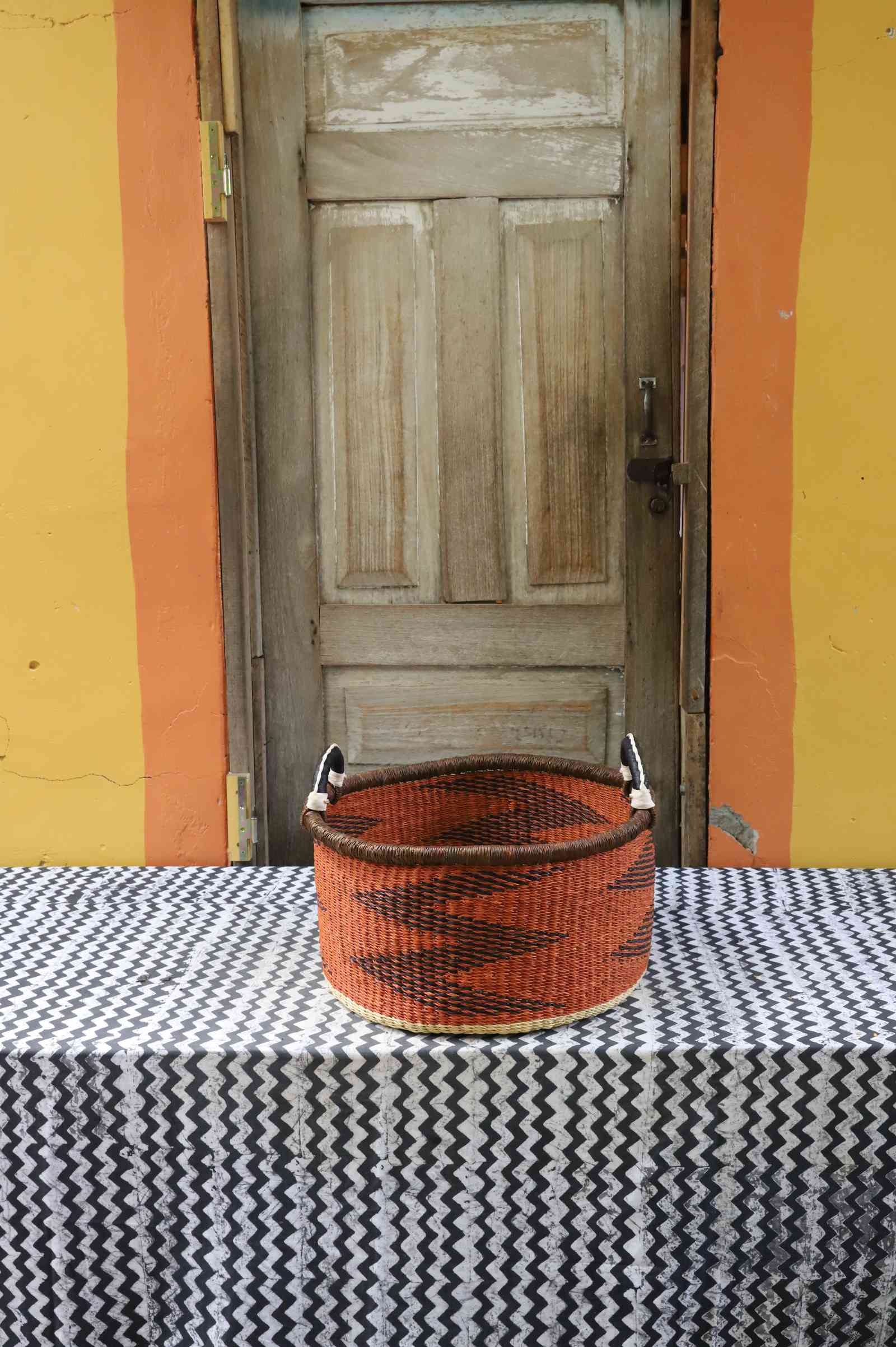 Small handwoven Bolga storage tub in dyed bold orange with a plain woven body and leather handles.