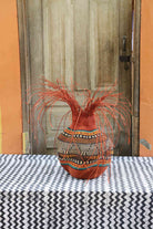 Handwoven Bolga Baobab-inspired basket in dyed rust-orange with a fine multicolour band and orange grass sprigs.