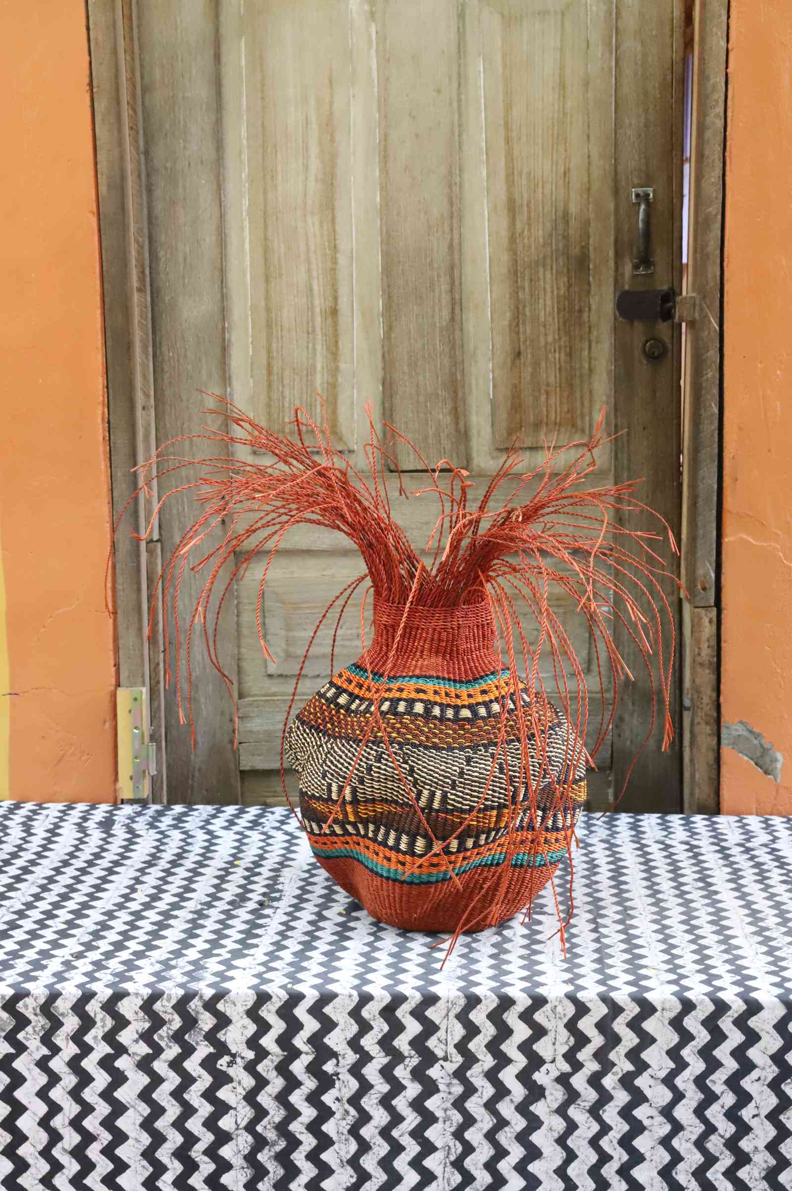 Handwoven Bolga Baobab-inspired basket in dyed rust-orange with a fine multicolour band and orange grass sprigs.