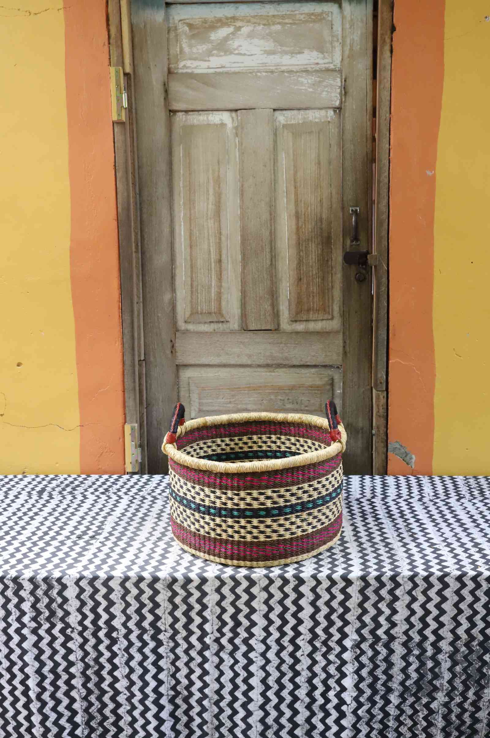Small handwoven Bolga storage tub in natural straw with red and dark banded stripes and leather handles.